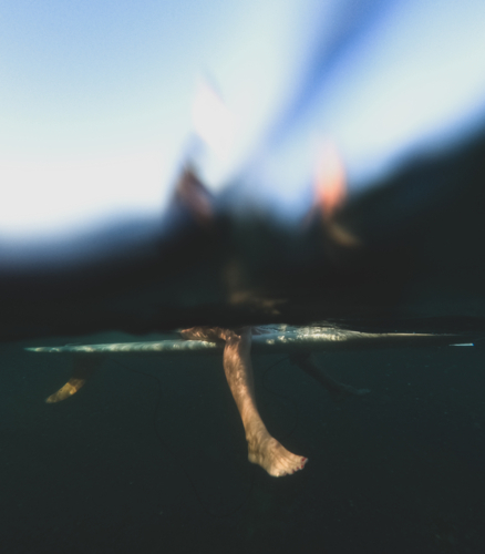 Underwater of females legs sitting on longboard single fin surfboard with good visibility - Australian Stock Image