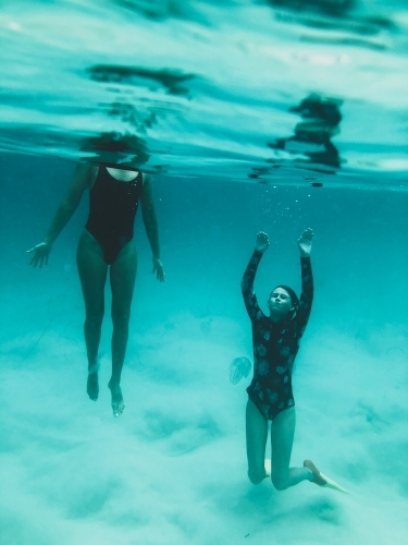 Underwater of two females, one diving under the surface in the ocean - Australian Stock Image