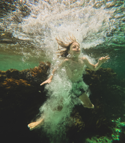 Underwater shot of young boy  underwater surrounded by bubbles after jumping in, reef inbackground - Australian Stock Image