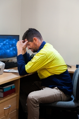 Unhappy tradie stressed out over paperwork in home office - Australian Stock Image