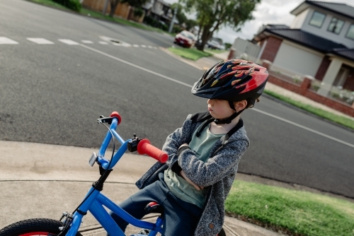 Unhappy young boy with his arms crossed on his bicycle; cycling around his neighbourhood - Australian Stock Image