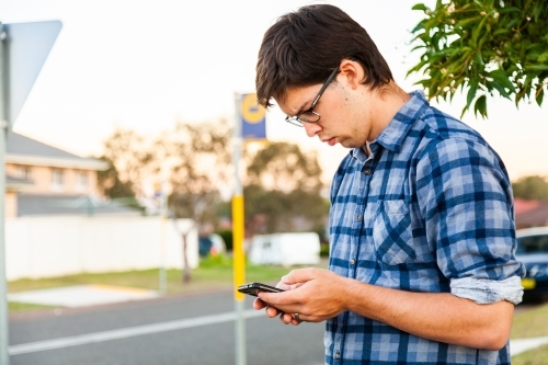 Uni student waiting at bus stop using mobile phone - Australian Stock Image