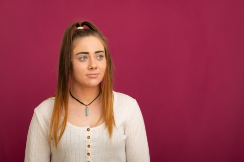 upper body of long-haired teen girl against dark pink background - Australian Stock Image