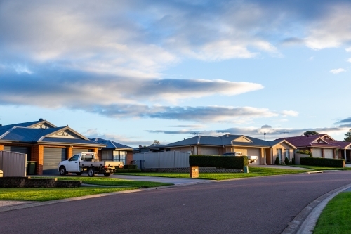 Utes in driveways of homes along quiet suburban street at sunset - Australian Stock Image