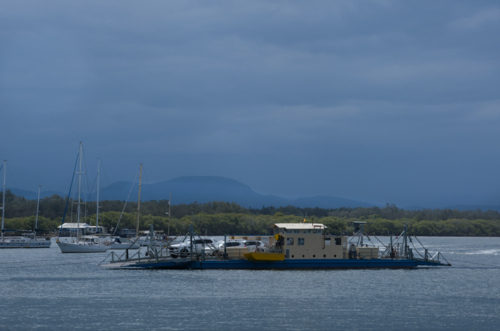 Vehicle ferry crossing river in sun, clouds and boats in background - Australian Stock Image
