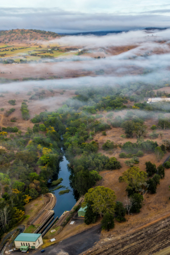Vertical Aerial image of the Glenbawn Dam wall with morning fog drifting through the valley - Australian Stock Image