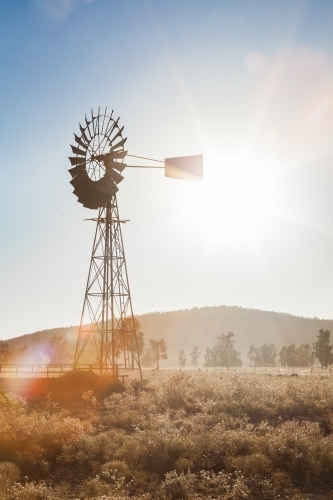 Vertical image of old windmill on farm, backlit with sun star flare