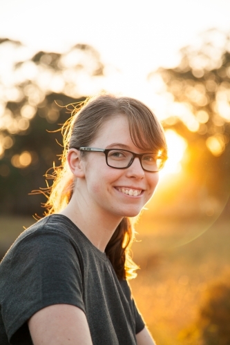 Vertical portrait of a young person with glasses smiling in rural Australia with golden sun flare - Australian Stock Image