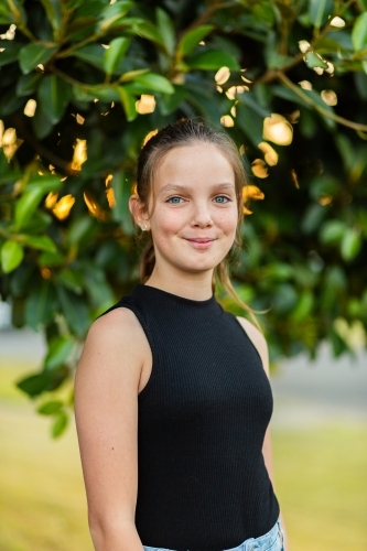 vertical portrait of smiling young tween girl against natural background of leaves - Australian Stock Image