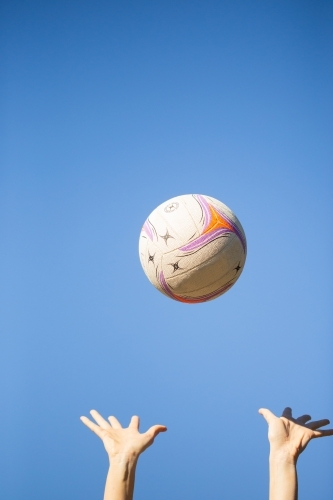 vertical shot of a ball thrown up in the air by two hands with clear skies in the background - Australian Stock Image