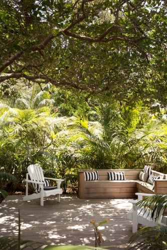 Vertical shot of a chair under a tree with a brown wooden couch and two white inclined chairs - Australian Stock Image