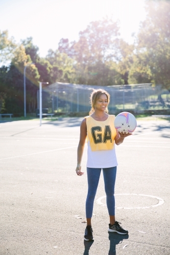 vertical shot of a Indian woman in sportswear holding a net ball on a sunny day - Australian Stock Image