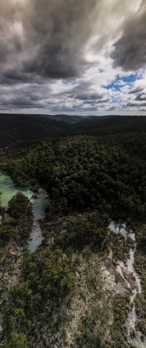 vertical shot of a lake surrounded by bush hills with green trees on a cloudy day with grey skies - Australian Stock Image