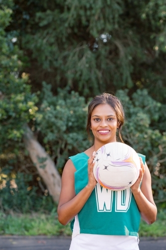 vertical shot of a tanned skin woman in sports in wear holding a net ball on a sunny day - Australian Stock Image