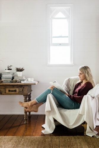 Vertical shot of a woman sitting on a couch while reading - Australian Stock Image