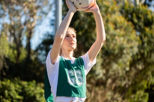 vertical shot of a young woman wearing sports clothes holding a ball up in the air on a sunny day - Australian Stock Image