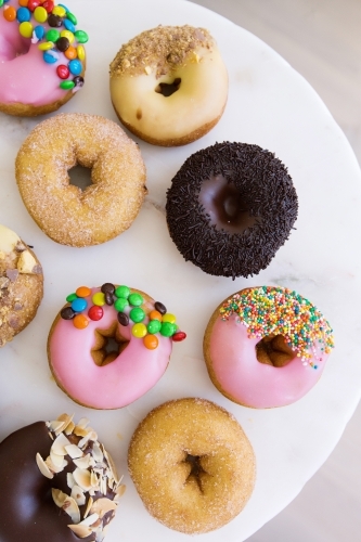 Vertical shot of different kinds of flavored donuts on a white plate.