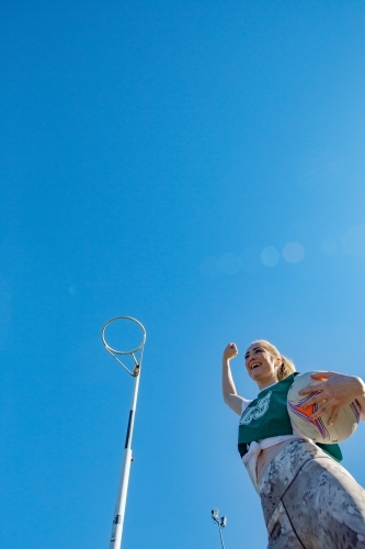 vertical shot of girl holding a net ball in between her hips while raising right arm in the air - Australian Stock Image