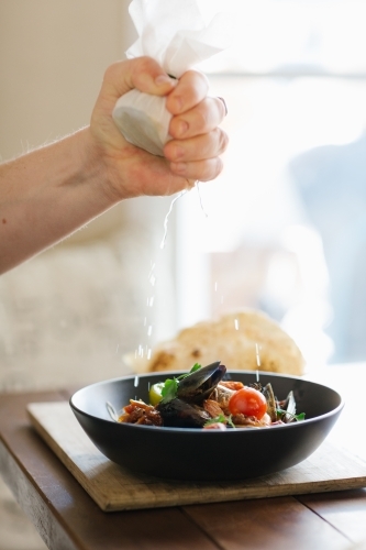 Vertical shot of hand squeezing a lemon wrapped in a white piece of cloth to a bowl of seafood