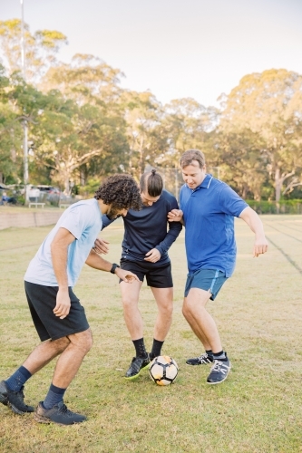 vertical shot of men playing soccer in the field on a sunny day with clear skies - Australian Stock Image