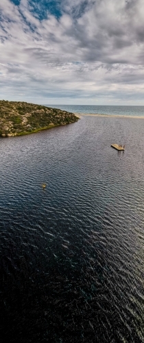 vertical shot of ocean water with wooden raft and an island under cloudy skies - Australian Stock Image