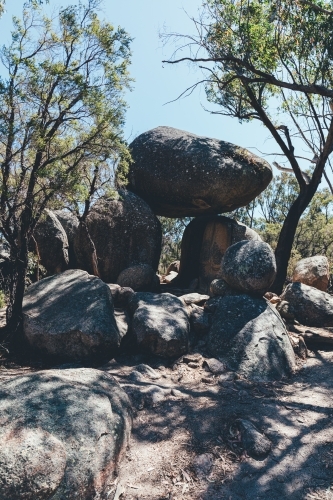 vertical shot of rocks stacked on top of each other with trees at the back on a sunny day - Australian Stock Image