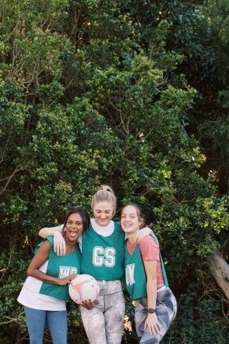 vertical shot of three young smiling women in sports clothes with one holding a net ball - Australian Stock Image