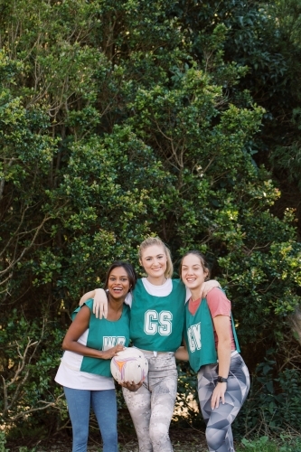 vertical shot of three young sporty women posing outdoors with one holding a net ball - Australian Stock Image
