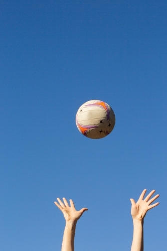 vertical shot of two hands raised up high and a ball thrown in the air with clear skies - Australian Stock Image
