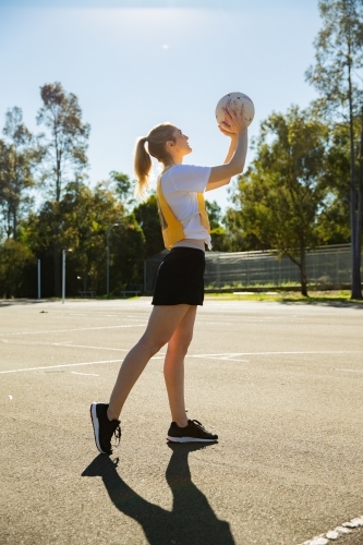 vertical shot of young woman holding a net ball in mid air on a sunny day with clear skies - Australian Stock Image