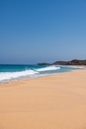 Vertical view looking along sandy beach with waves towards a headland - Australian Stock Image