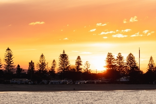 Vibrant orange sunset over caravan park at Stockton NSW with view across the water - Australian Stock Image
