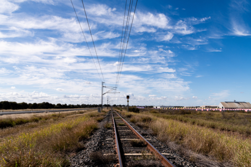 view along railway tracks lined with cotton bales and cloud patterns in blue sky - Australian Stock Image