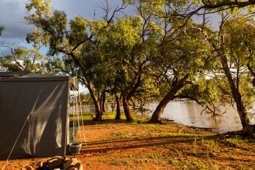 View of a campsite beside  an outback lagoon in early morning golden light - Australian Stock Image