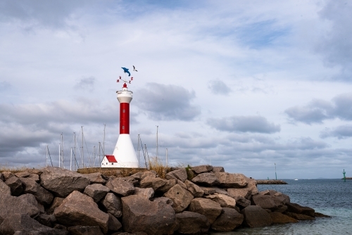 View of a miniature lighthouse on a rocky groyne with dramatic sky and harbour