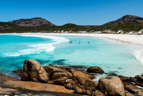 View of a white sandy beach with people swimming in aqua blue water - Australian Stock Image
