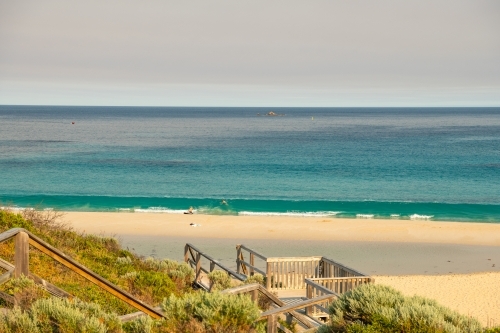 View of beach with people in water from upper boardwalk and staircase - Australian Stock Image