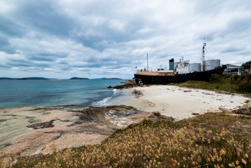 View of beached old whaling boat with sand beach and massed seed heads in foreground. - Australian Stock Image