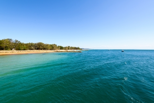 View of blue green water and island beach with clear blue sky - Australian Stock Image