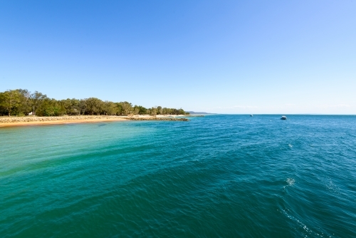 View of blue green water and island beach with clear blue sky