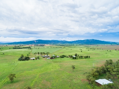 View of distant farm home area with house and sheds among green paddocks - Australian Stock Image