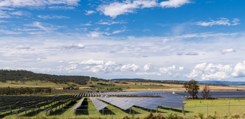 View of large scale solar farm in rural setting with blue sky and cloud formations