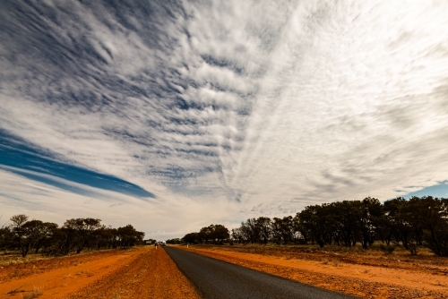 View of long straight bitumen road to horizon with dramatic cloud formations - Australian Stock Image
