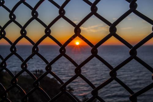 view of sunrise over the ocean through a wire fence
