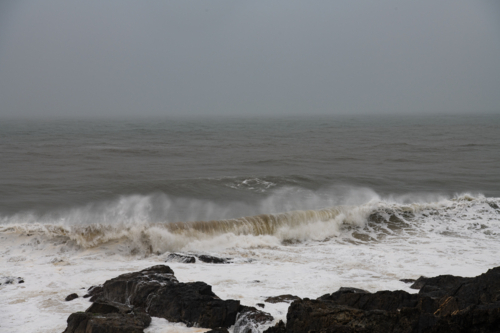 View of wave breaking with spray and froth,  and rocks in the foreground - Australian Stock Image