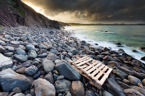 View out to ocean from a rocky shoreline with a washed up pallet on the rocks - Australian Stock Image