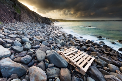 View out to ocean from a rocky shoreline with a washed up pallet on the rocks