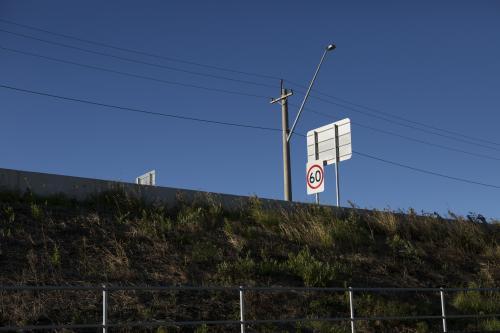 View up grassy verge towards road signs and power lines - Australian Stock Image