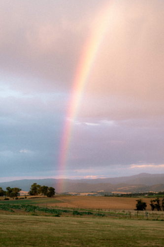 Vivid rainbow arching across moody sky of the countryside - Australian Stock Image