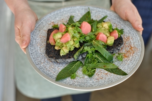 Waiter holding healthy avocado on toast meal on plate